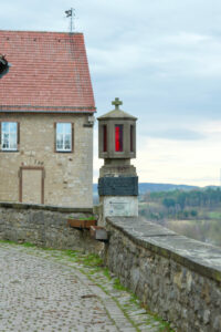 Gedenkleuchte für Josef Wirmer und Wilhelm-Emanuel von Ketteler. Im Hintergrund sieht man die Westseite des Mittelbaus des ehem. Dominikanerklosters mit der  antijüdischen Chimäre
