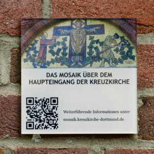 Ein Schild an einer Backsteinmauer zeigt das Bild eines Mosaiks mit drei Figuren und einem QR-Code. Der Text auf Deutsch lautet: Das Mosaik über dem Haupteingang der Kreuzkirche und bietet einen Link für weitere Informationen. (Text mit KI erstellt)