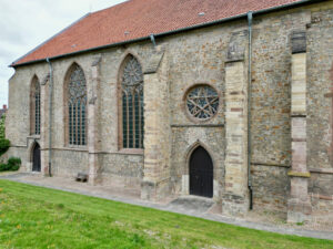 Außenansicht einer historischen Steinkirche mit hohen gewölbten Buntglasfenstern, einer runden Fensterrose und einer dunklen Holztür auf einer Rasenfläche. (Text mit KI erstellt)
