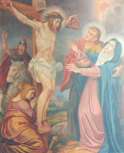 Ein Gemälde zeigt die Kreuzigung Jesu, der eine Dornenkrone auf einem Holzkreuz trägt. Drei Trauernde, darunter eine Frau in Blau und Weiß, stehen zu seinen Füßen, während ein römischer Soldat zusieht. Im Hintergrund ist ein bewölkter Himmel zu sehen. (Text mit KI erstellt)