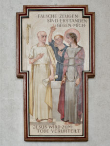 Eine gemalte religiöse Tafel zeigt Jesus, der mit einem Seil gefesselt neben zwei Männern steht. Der eine Mann hält eine Schriftrolle und gestikuliert anklagend. Der deutsche Text darüber und darunter bezieht sich auf die Verurteilung Jesu zum Tode durch falsche Zeugen. (Text mit KI erstellt)