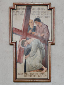 Eine gemalte religiöse Szene in einem kreuzförmigen Rahmen zeigt Jesus, der unter dem Gewicht eines großen Kreuzes fällt, während zwei Männer neben ihm stehen. Über und unter der Szene steht ein deutscher Text. (Text mit KI erstellt)