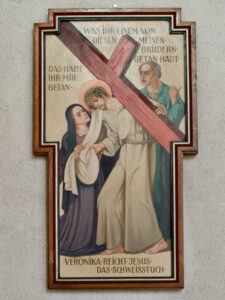 Ein religiöses Gemälde von Veronika, die Jesus das Gesicht abwischt, während er das Kreuz trägt, mit einem anderen Mann hinter ihnen. Ein deutscher Text und ein Rahmen in Form eines Kreuzes umgeben die Szene. (Text mit KI erstellt)