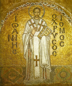 Ein goldenes byzantinisches Mosaik zeigt eine religiöse Figur mit Heiligenschein in weißem Gewand, die ein Buch hält und eine segnende Geste macht. Griechische Inschriften erscheinen auf beiden Seiten vor einem schimmernden Goldhintergrund. (Text mit KI erstellt)