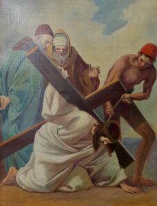 Eine Person in weißem Gewand, die eine Dornenkrone trägt, kniet nieder und trägt ein großes Holzkreuz. Drei Männer stehen um sie herum, einer hilft ihr, zwei beobachten sie mit ernster Miene. Im Hintergrund ist der Himmel zu sehen. (Text mit KI erstellt)