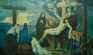 Ein Gemälde stellt die Kreuzigung Jesu dar, mit Trauernden, die sich um das Kreuz versammelt haben. Jesus hängt am Kreuz, während Gestalten in Gewändern vor einem blau-grünen Hintergrund stehen oder knien und trauern. (Text mit KI erstellt)
