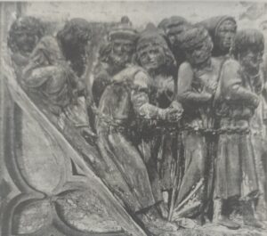 Ein Steinrelief zeigt eine Darstellung von Menschen, die eng beieinander stehen, mit verzweifelten Gesichtern und gefesselten Händen, die auf eine Gefangenschaft hindeuten. Die Figuren tragen mittelalterliche Kleidung und erinnern an die düsteren Ereignisse des Jahres 1476. (Text mit KI erstellt)