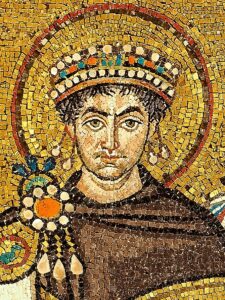 Mosaikkunstwerk, das eine königliche Figur mit juwelenbesetzter Krone und Heiligenschein darstellt, gekleidet in prunkvolle Gewänder vor einem goldenen Hintergrund; der Stil lässt auf einen byzantinischen Kaiser schließen. (Text mit KI erstellt)