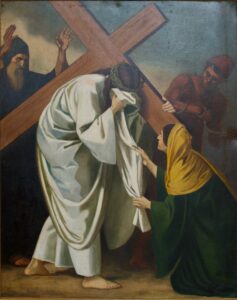 Eine Frau kniet nieder und bietet Jesus, der ein großes Holzkreuz und eine Dornenkrone trägt, ein Tuch an, während im Hintergrund zwei Männer stehen. (Text mit KI erstellt)