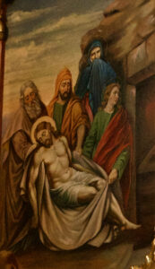 Ein Gemälde zeigt vier Figuren, die den in ein weißes Tuch gehüllten Leichnam Jesu tragen. Zwei Frauen und zwei Männer assistieren mit feierlicher Miene und gedämpfter Kleidung vor einem düsteren Hintergrund. (Text mit KI erstellt)