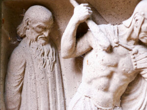 Steinrelief mit einem bärtigen Mann mit ernster Miene auf der linken Seite und einem muskulösen Mann mit freiem Oberkörper auf der rechten Seite, der eine Waffe oder einen Stab über die Schultern legt. (Text mit KI erstellt)