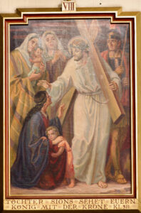 Ein Gemälde zeigt Jesus, der ein Kreuz trägt und einer Frau und einem Kind die Hand zum Trost reicht. Zwei Frauen stehen hinter ihr, und ein Soldat steht neben Jesus. Die Szene hat warme Farben und einen goldenen Rahmen mit deutschem Text am unteren Rand. (Text mit KI erstellt)