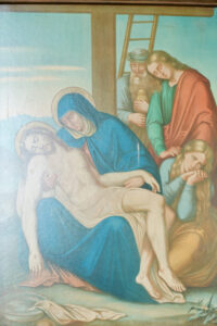 Ein Gemälde der Pietà zeigt Maria, die den leblosen Körper Jesu hält, während hinter ihr drei Trauernde stehen, darunter zwei Frauen und ein Mann. Im Hintergrund lehnt eine Leiter, die die Kreuzigungsszene symbolisiert. (Text mit KI erstellt)