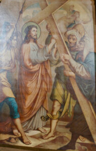 Ein Gemälde, das Jesus zeigt, der ein Holzkreuz trägt und von mehreren Männern umgeben ist. Jesus hat einen Heiligenschein und trägt ein langes Gewand, während andere ihm helfen oder ihn anleiten. Die Szene ist in einem biblischen Kontext angesiedelt. (Text mit KI erstellt)