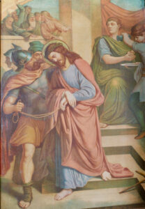 Ein Gemälde zeigt Jesus, der gefesselt ist und eine Dornenkrone trägt, während er von einem römischen Soldaten geführt wird. Andere Figuren schauen zu oder schreiben im Hintergrund und stellen eine Szene aus dem Prozess gegen Jesus vor seiner Kreuzigung dar. (Text mit KI erstellt)