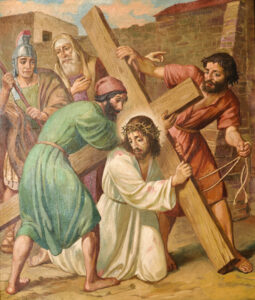 Ein Gemälde zeigt Jesus mit einer Dornenkrone und einem Holzkreuz, umgeben von mehreren Männern, darunter ein römischer Soldat, während er zu Boden fällt. Ein Mann hilft, das Kreuz zu heben, während andere zusehen. (Text mit KI erstellt)