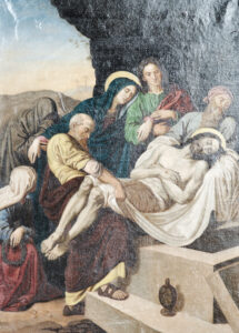 Ein Gemälde zeigt den Leichnam Jesu, der von mehreren Trauernden, darunter die traurig wirkende Maria, in ein Grab gelegt wird. Die Szene ist düster und in gedämpften Farben gehalten, und neben dem Eingang des Grabes steht ein Fläschchen. (Text mit KI erstellt)