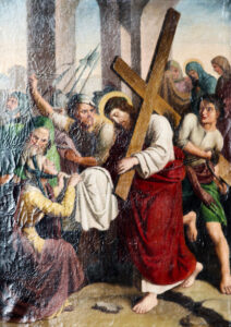 Jesus trägt ein Holzkreuz, während eine Frau vor ihm kniet und ein Tuch hält. Eine Menschenmenge umgibt sie, einige sehen verzweifelt aus, inmitten von Steinbögen mit blauem Himmel im Hintergrund. (Text mit KI erstellt)