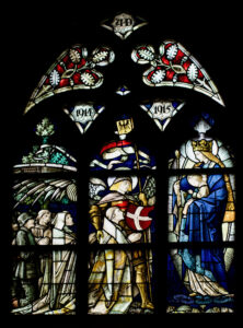 Glasfenster mit Figuren in Rüstungen, Menschen, die sich aufstellen, und einer Heiligenfigur, die ein Kind hält. Das Fenster ist mit den Jahreszahlen 1914 und 1915 beschriftet, wobei die Farben Rot und Blau das Design dominieren. (Text mit KI erstellt)