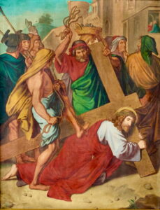 Ein Gemälde zeigt Jesus, der ein Holzkreuz trägt, umgeben von römischen Soldaten und Umstehenden. Jesus liegt auf dem Boden, trägt eine Dornenkrone und ein rotes Gewand, und die Soldaten drängen ihn vorwärts. (Text mit KI erstellt)