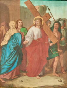 Jesus, der eine Dornenkrone und ein rotes Gewand trägt, geht mit einem Holzkreuz, umgeben von römischen Soldaten und Anhängern, von denen ihm einer die Hand reicht, vor dem Hintergrund der antiken Stadtmauern. (Text mit KI erstellt)