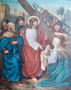 Ein Gemälde zeigt Jesus, der ein Holzkreuz trägt, umgeben von Soldaten und Anhängern. Eine Frau kniet mit einem Tuch in der Hand vor ihm, während andere mit Sorge und Kummer zusehen. (Text mit KI erstellt)