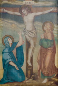 Ein Gemälde zeigt Jesus am Kreuz, über ihm ein Schild mit der Aufschrift INRI. Zwei Frauen, traditionell Maria und Maria Magdalena, stehen und knien trauernd am Fuß des Kreuzes vor einem bewölkten Himmel. (Text mit KI erstellt)