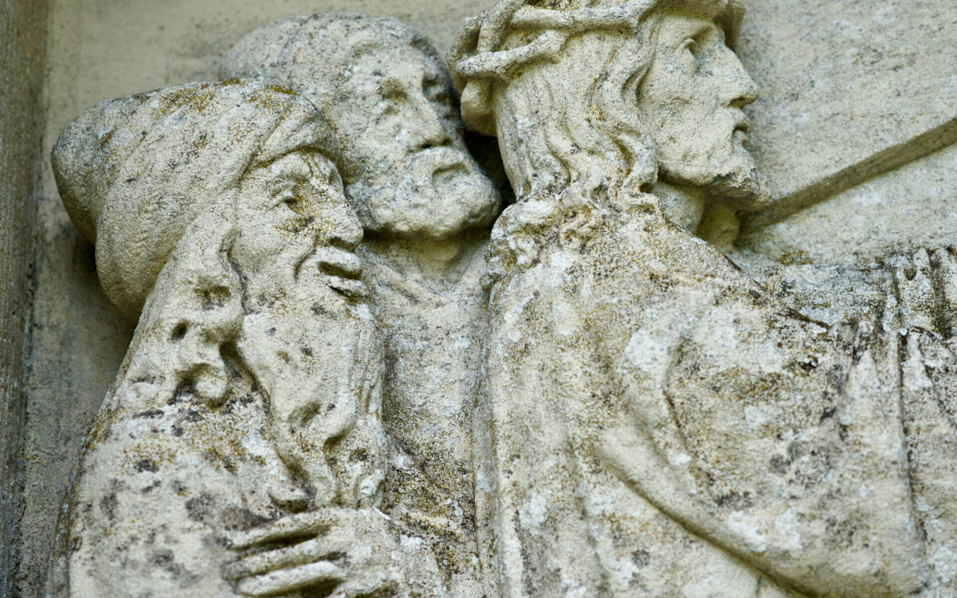 Verwittertes Steinrelief mit der Darstellung dreier bärtiger Männer in Gewändern, von denen einer eine Dornenkrone trägt, die alle eng beieinander stehen und nach rechts blicken, was auf eine religiöse oder biblische Szene schließen lässt. ( )