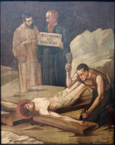 Ein Gemälde, das die Kreuzigung Jesu darstellt. Jesus liegt auf einem Holzkreuz, ein Mann schlägt ihm einen Nagel in die Hand, während ein anderer ein Schild mit der Aufschrift „Jesus Nazarenus Rex Judaeorum“ hochhält. Eine dritte Gestalt steht hinter ihnen und beobachtet das Geschehen. (Text mit KI erstellt)
