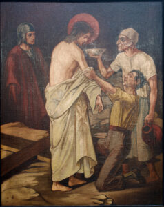 Ein Gemälde zeigt Jesus im Stehen, in ein weißes Tuch gehüllt und mit einem Heiligenschein. Zwei Männer reichen ihm etwas zu trinken und stützen ihn, während ein weiterer Mann in Rüstung zusieht. Zu Jesu Füßen liegt ein Holzgerüst. (Text mit KI erstellt)