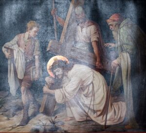 Ein Gemälde zeigt Jesus, wie er ein großes Holzkreuz trägt und zu Boden fällt, wobei sein Kopf von einem Heiligenschein umgeben ist. Drei Männer umringen ihn: Einer hält ein Tuch in der Hand, ein anderer stützt das Kreuz, und der dritte steht mit einem Stock da. (Text mit KI erstellt)