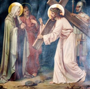Jesus trägt ein hölzernes Kreuz und eine Dornenkrone, während zwei Frauen besorgt daneben stehen. Im Hintergrund steht ein römischer Soldat mit einem Speer in der Hand vor einem dunklen Hintergrund. Die Szene erinnert an eine Station des Kreuzwegs. (Text mit KI erstellt)