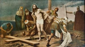 Ein Gemälde zeigt, wie Jesus vor der Kreuzigung seiner Kleidung beraubt wird, umgeben von römischen Soldaten und Schaulustigen, während ein großes Holzkreuz auf dem Boden liegt. (Text mit KI erstellt)