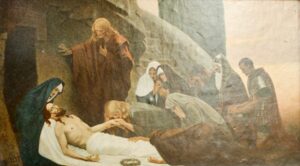 Eine Gruppe trauert um den Leichnam Jesu, der auf einem weißen Leichentuch aufgebahrt ist. Mehrere Gestalten, darunter verschleierte Frauen und Männer in Gewändern und Rüstungen, haben sich in Trauer versammelt. Daneben liegt eine Dornenkrone. Die Szene wirkt düster und andächtig. (Text mit KI erstellt)