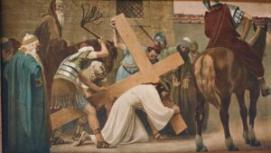 Ein Mann in weißer Gewandung, der ein großes Holzkreuz trägt, sinkt auf die Knie, umringt von Soldaten und Schaulustigen. Ein Soldat hebt eine Peitsche, während eine weitere Gestalt zu Pferd das Geschehen beobachtet. Die Szene wirkt historisch und düster. (Text mit KI erstellt)