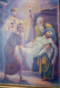 Drei Männer tragen den leblosen Körper Jesu, der in ein weißes Tuch gewickelt ist. Ein Mann hält eine Fackel in der Hand, die die Szene erhellt. Die Stimmung ist düster, und der Hintergrund lässt auf ein Grab oder eine Gruft schließen. (Text mit KI erstellt)