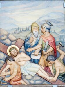 Ein religiöses Kunstwerk zeigt vier Männer, die Jesus kreuzigen, der eine Dornenkrone trägt und am Kreuz liegt. Zwei Männer halten Nägel und einen Hammer in der Hand, ein weiterer trägt eine Rüstung und hält ein Schwert, während der vierte zusieht. Die Szene spielt im Freien vor dem Hintergrund von Hügeln. (Text mit KI erstellt)