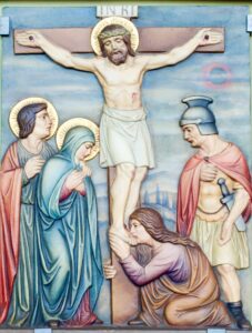 Religiöses Kunstwerk, das Jesus am Kreuz mit drei trauernden Frauen zeigt, von denen eine kniet und seine Füße umarmt, während daneben ein römischer Soldat mit einem Speer steht. Alle Figuren außer dem Soldaten sind mit goldenen Heiligenscheinen umgeben. Im Hintergrund sind ein blauer Himmel und eine ferne Landschaft zu sehen. (Text mit KI erstellt)