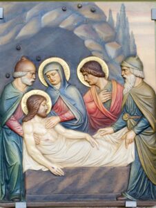 Religiöses Gemälde, auf dem vier Personen eine leblose Gestalt umgeben und um sie trauern, die auf einer Steinplatte liegt; alle sind mit goldenen Heiligenscheinen dargestellt, vor einem felsigen Hintergrund. (Text mit KI erstellt)