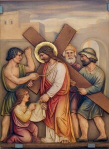 Religiöses Gemälde, das Jesus zeigt, wie er ein hölzernes Kreuz trägt, umgeben von drei Männern und einer knienden Frau. Ein Mann hilft ihm, ein anderer schaut zu, während die Frau nach Jesus greift. Im Hintergrund sind Gebäude im antiken Stil zu sehen. (Text mit KI erstellt)