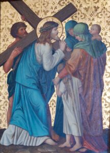 Jesus trägt ein hölzernes Kreuz, ist in ein blaues Gewand gekleidet und trägt eine Dornenkrone; er hält inne, um Frauen und Kinder zu trösten. Ein Mann stützt das Kreuz, und goldene Blumenmuster zieren den Hintergrund. Die Szene ist feierlich und bewegend. (Text mit KI erstellt)