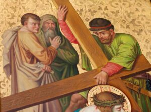 Ein Mann in grüner Kleidung trägt ein großes Holzkreuz; zwei Männer, von denen einer eine Kapuze trägt, stehen neben ihm. Unterhalb ist teilweise eine weitere Gestalt mit einer Dornenkrone zu erkennen. Der Hintergrund ist reich verziert und goldfarben mit einem Blumenmuster. (Text mit KI erstellt)
